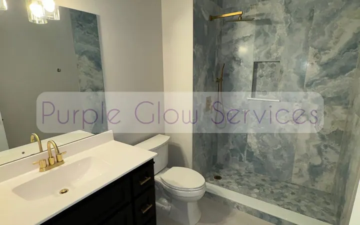 Spotless bathroom with a marble-look shower surround and gold fixtures cleaned by Purple Glow Services