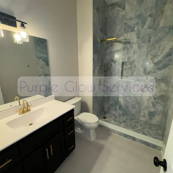 Spotless bathroom with a marble-look shower surround and gold fixtures cleaned by Purple Glow Services