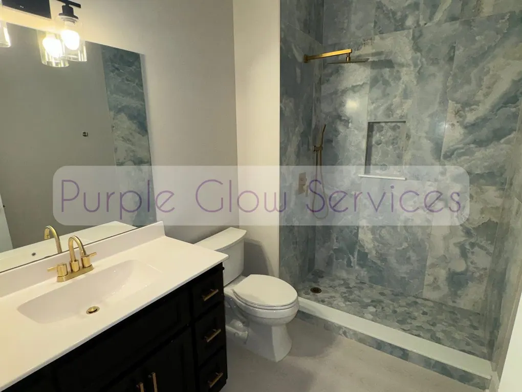 Spotless bathroom with a marble-look shower surround and gold fixtures cleaned by Purple Glow Services